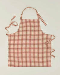 The Essential Check Apron in Blush/Terracotta by Hawkins New York is laid flat on a light background—an ideal cotton kitchen gift with neck and waist ties for any home chef.