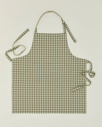 The Hawkins New York Essential Check Apron in Sage/Olive features a cotton check grid design, shown laid flat with adjustable halter neck and waist ties extended outward.