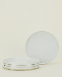 Four Hawkins New York Essential Dinner Plates in Bone are shown—three stacked and one upright behind them—displayed against a simple background; this sleek set of 4 stoneware plates is perfect for any table setting.