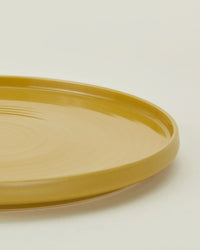 A close-up of the Hawkins New York Essential Dinner Plates in Mustard (Set of 4), featuring round, yellow ceramic plates with a smooth, glossy finish against a plain background.