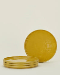 Four Hawkins New York Essential Dinner Plates in Mustard (set of 4) are stacked, with one plate upright behind the group, all set against a plain light background.