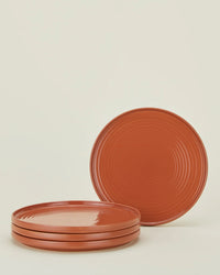 The Essential Dinner Plates in Terracotta – Set of 4 by Hawkins New York features stylish stoneware plates, with three stacked and one upright, displayed against a plain light background.