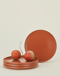 Four Essential Dinner Plates in Terracotta from Hawkins New York, stacked with two golden beets on top and one plate standing upright in the background, all set against a plain light backdrop. Set includes four plates.