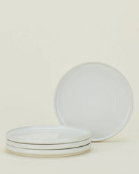 Four bone-colored ceramic plates from the Hawkins New York Essential Dinnerware 16 Piece Set are displayed—three stacked, one upright—against a light background, making them an ideal choice for any table.