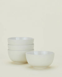 Four white ceramic bowls from the Hawkins New York Essential Dinnerware in Bone – 16 Piece Set, with three stacked on the left and one placed separately on the right, set against a plain light background.