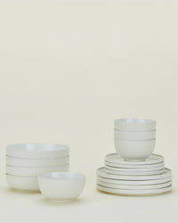A set of stacked white ceramic bowls and plates from the Hawkins New York Essential Dinnerware in Bone 16 Piece Set is arranged neatly against a plain light background.