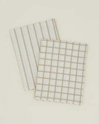 A pair of Hawkins New York Essential Dish Towels in Flax/Ivory—one striped, one grid patterned—crafted from Oeko-Tex cotton, displayed folded on a light surface.