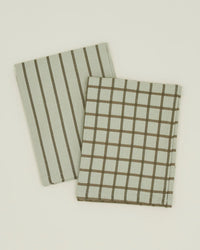 Two folded Hawkins New York Essential Dish Towels in Olive/Sage, set of 2, featuring striped and grid patterns, rest on a light background.
