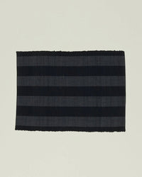 The Essential Floor Mat in Black by Hawkins New York features alternating black and dark gray stripes, is rectangular, crafted from recycled fiber, fully machine washable, and displayed on a plain light background.