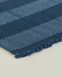 The Essential Floor Runner in Navy by Hawkins New York features alternating dark and light blue horizontal stripes on a light background, crafted from recycled fibers.