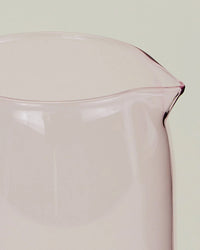 A close-up of the Hawkins New York Essential Glassware Pitcher in Blush, crafted from borosilicate glass and featuring a spout, set against a pale background.
