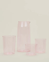 A Hawkins New York Essential Glassware - Pitcher in Blush and three matching translucent pink cups are displayed against a plain, light background.