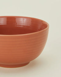 A close-up of a round, orange ceramic bowl with a glossy finish—part of Hawkins New York’s Essential Large Bowls in Terracotta, Set of 4—shown against a light background.