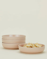 A set of four blush Essential Low Bowls by Hawkins New York is stacked with another matching bowl in front filled with tortilla chips, all against a simple light background—elegant stoneware dinnerware for any occasion.