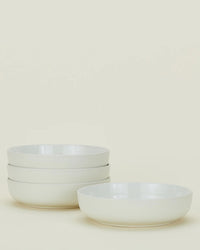 Four Hawkins New York Essential Low Bowls in Bone are displayed on a plain light background—three stacked on the left and one placed separately on the right.