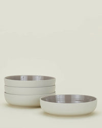 The Essential Low Bowls in Light Grey - Set of 4 by Hawkins New York are stacked in two groups, showing their stoneware construction with glossy interiors and matte exteriors against an off-white background.