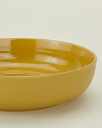 A set of four Essential Low Bowls in Mustard by Hawkins New York features a smooth, glossy ceramic finish—an ideal addition to any stoneware dinnerware collection.