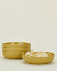 Four Hawkins New York Essential Low Bowls in Mustard are stacked on the left, with one holding tortilla chips on the right, all against a light backdrop—a stylish showcase of this stoneware dinnerware set.
