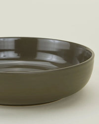 A close-up of the Essential Low Bowls in Olive - Set of 4 by Hawkins New York, featuring smooth, glossy stoneware with a dark green finish, elegantly displayed against a light background.