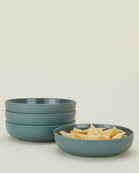 Four Peacock Essential Low Bowls by Hawkins New York—three stacked, one filled with tortilla chips—showcase stylish stoneware against a light background.