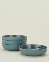 Four Essential Low Bowls in Peacock from Hawkins New York are stacked on the left, with one matching stoneware bowl set alone to the right, all displayed against a plain off-white background.