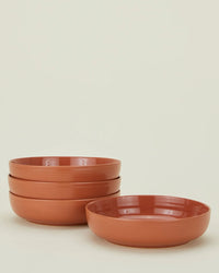A set of four terracotta Essential Low Bowls by Hawkins New York is stacked on a plain light background, with one bowl placed beside the stack.