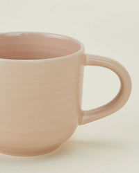 A close-up of a blush ceramic Essential Mug with a rounded handle from the Hawkins New York Essential Mugs in Blush - Set of 4, shown against a plain, off-white background.