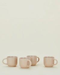 Four blush Essential Mugs by Hawkins New York are arranged in a row against a neutral background, highlighting this elegant set of 4 stoneware mugs.