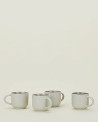 Four light grey stoneware mugs with handles from Hawkins New Yorks Essential Mugs set are arranged in a row on a light surface against an off-white background—timeless, elegant, and dishwasher safe.