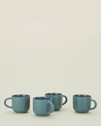 The Hawkins New York Essential Mugs in Peacock - Set of 4 feature a sleek blue stoneware design, displayed in a row on a light surface against a plain cream background.