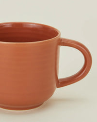 A close-up of the Hawkins New York Essential Mugs in Terracotta—set of 4—features a large handle and a stoneware-inspired design, set against a plain light background.