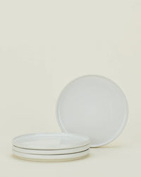 Four Essential Salad Plates in Bone by Hawkins New York are arranged with three stacked horizontally and one upright behind them, set against a plain light background.