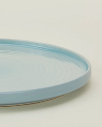 A close-up of a Hawkins New York Essential Salad Plate in Sky, featuring smooth stoneware with a glossy finish and slightly raised rim, shown on a pale background. Set includes 4 plates.