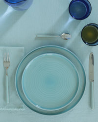 A neatly arranged place setting features Hawkins New York Essential Salad Plates in Sky, silverware, a light blue napkin, three drinking glasses, and a light blue tablecloth.