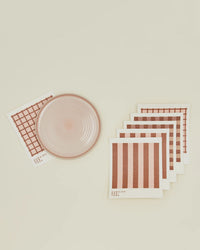 A round pink ceramic plate sits beside a set of Hawkins New York Essential Swedish Dishcloths in Blush/Terracotta (set of 6), arranged neatly on a cream surface—perfect for stylish, eco-friendly kitchen use.