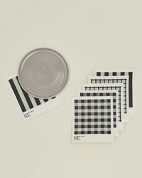 The Hawkins New York Essential Swedish Dishcloths in Light Grey/Black, set of 6, are arranged in a fan shape beside a round gray plate on a light background.