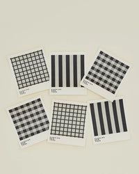 Six Essential Swedish Dishcloths in Light Grey/Black by Hawkins New York feature various black and white patterns. This eco-friendly set of 6 is perfect for stylish kitchen cleaning.