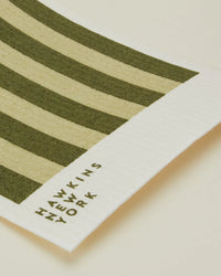 A close-up of Hawkins New York Essential Swedish Dishcloths in Olive/Sage—set of 6—shows “HAWKINS NEW YORK” printed on the white border, highlighting the eco-friendly design.