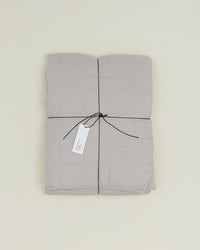 The Simple Linen Quilt in Light Grey by Hawkins New York, stonewashed and folded, is tied with a black string and a white tag, set on a plain light background.