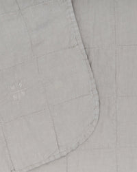 Close-up of the Simple Linen Quilt in Light Grey by Hawkins New York, featuring a stitched grid pattern and an embroidered HN NY logo on one corner.