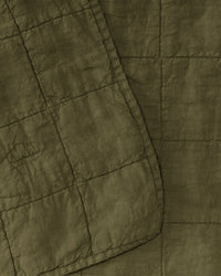 Close-up of the Simple Linen Quilt in Olive by Hawkins New York, featuring green quilted fabric with visible grid stitching and a small embroidered detail near the edge.