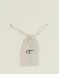 A compact, light-colored drawstring pouch with Hawkins New York on the front, ideal for holding your Simple Measuring Spoons in Black, shown against a plain background.