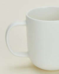A close-up of a Hawkins New York Simple Porcelain Mug, part of a set of 4, featuring a curved handle and shown against a neutral light background.