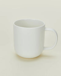 The Hawkins New York Simple Porcelain Mugs - Set of 4 feature a classic white design with simple handles, set against a light beige background—ideal for those who appreciate timeless style.