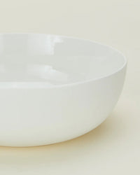 A close-up of the Simple Porcelain Serving Bowl by Hawkins New York, featuring a round shape, smooth edges, and a glossy white porcelain finish on a light, neutral background.