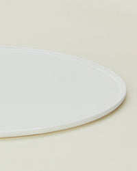 Close-up of the Hawkins New York Simple Porcelain Serving Platter—partially visible—showcasing its clean, white design against a light beige background.
