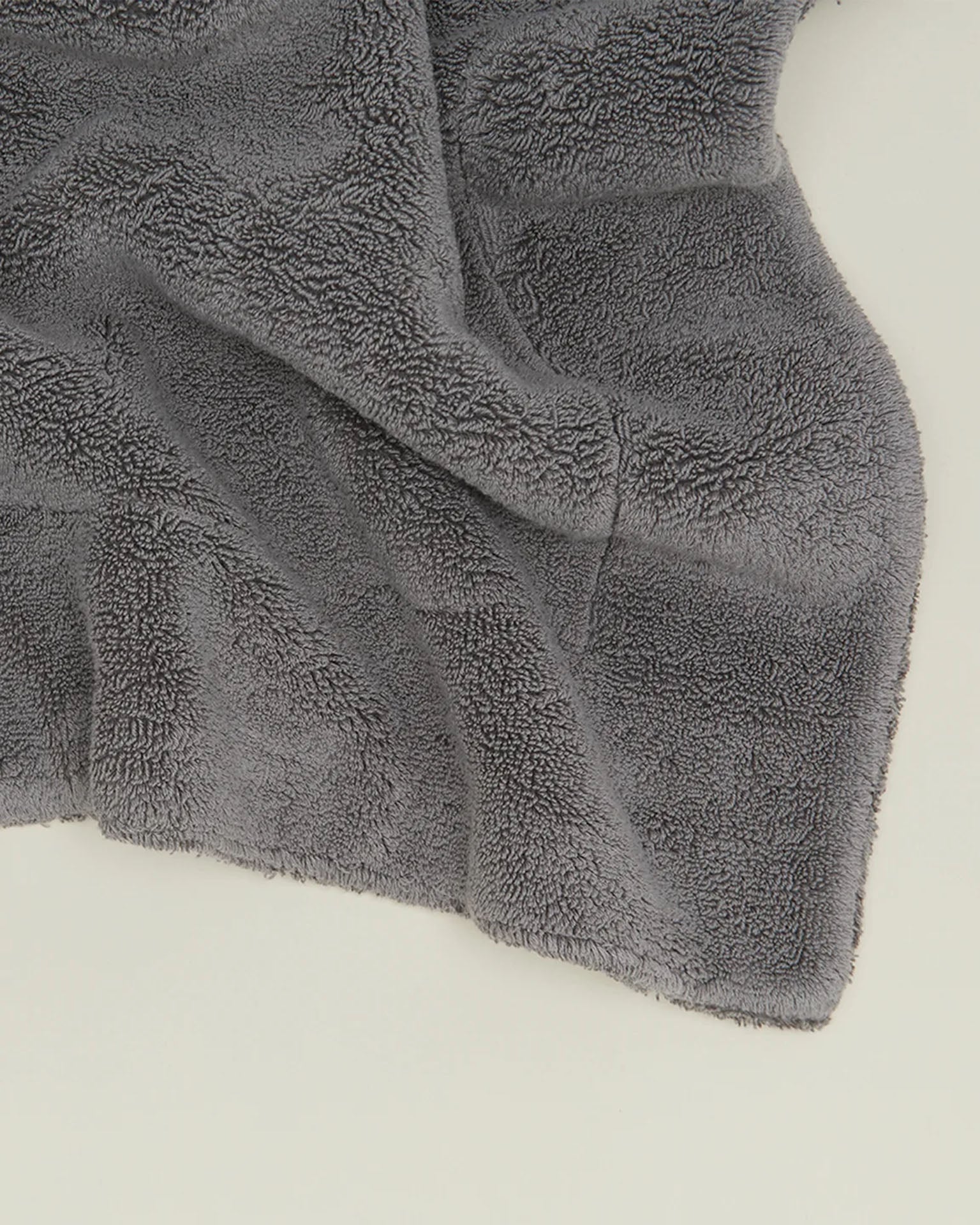 A close-up of the Hawkins New York Simple Terry Bath Mat in Dark Grey shows its soft, textured cotton fabric resting on a flat white surface.