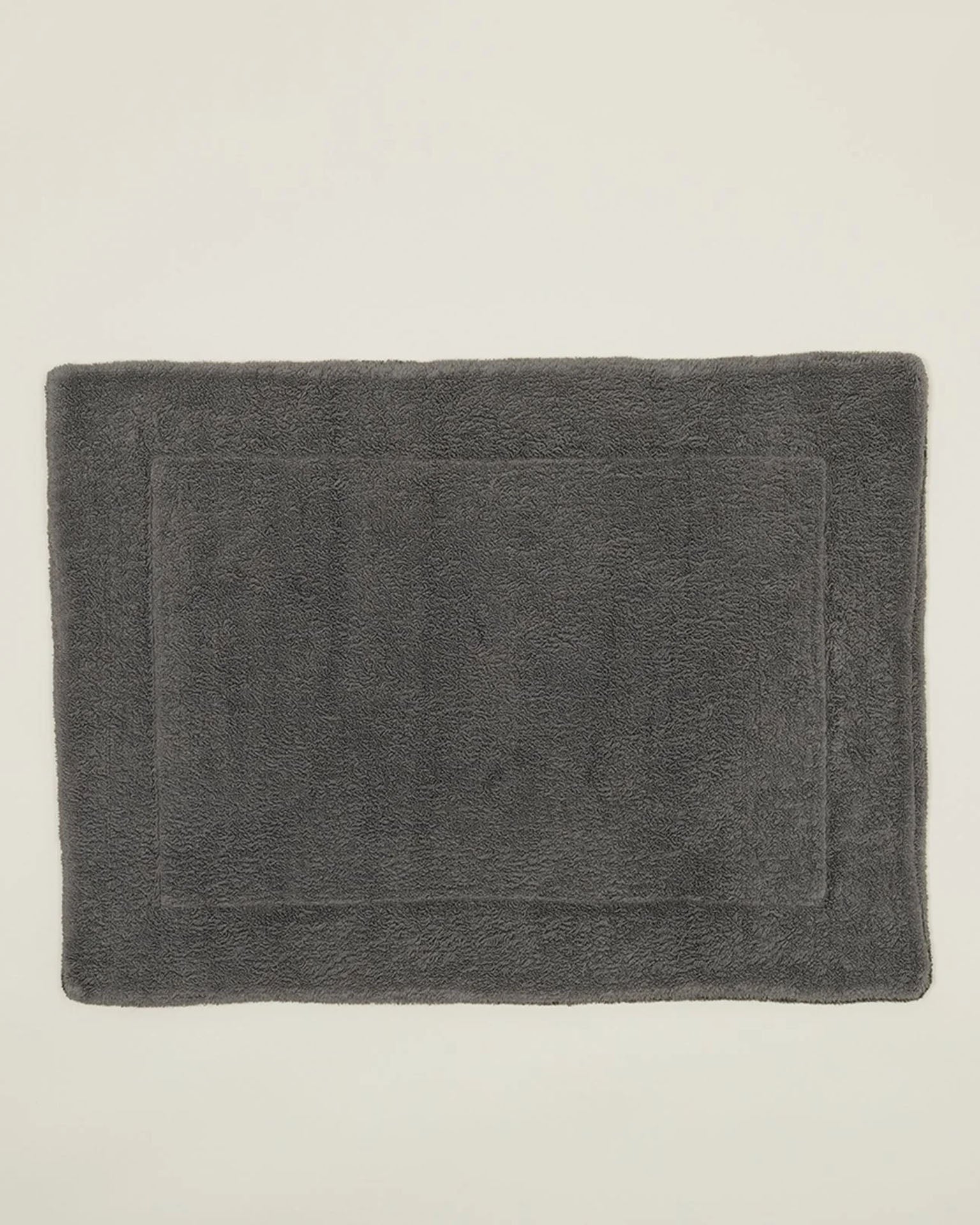 A Simple Terry Bath Mat in Dark Grey by Hawkins New York, made from soft cotton with a subtle border, is displayed on a plain light-colored surface.
