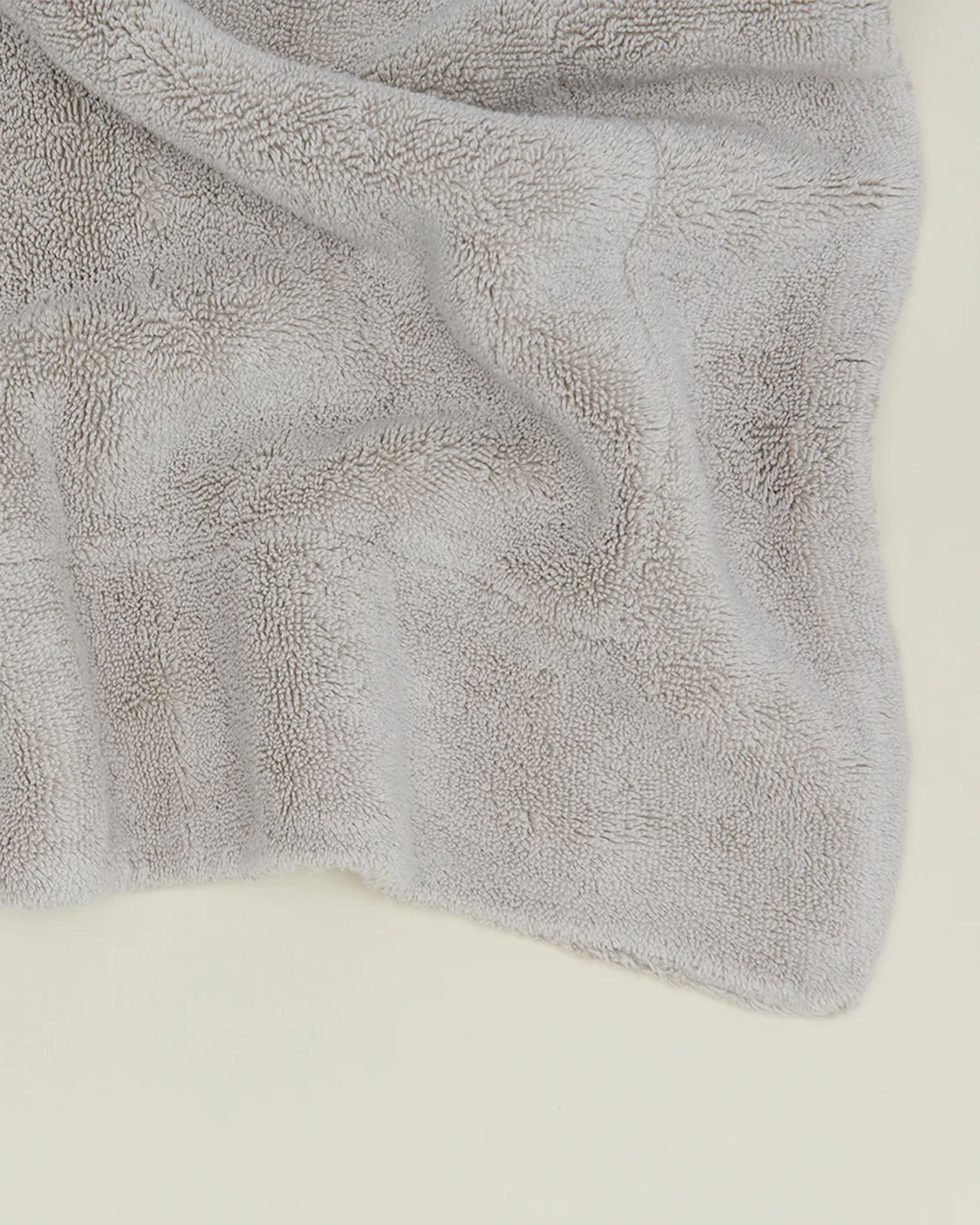 A close-up of the Simple Terry Bath Mat in Light Grey from Hawkins New York, showing its soft and fluffy cotton texture on a light surface.