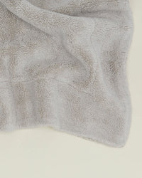 A close-up of the Simple Terry Bath Mat in Light Grey from Hawkins New York, showing its soft and fluffy cotton texture on a light surface.